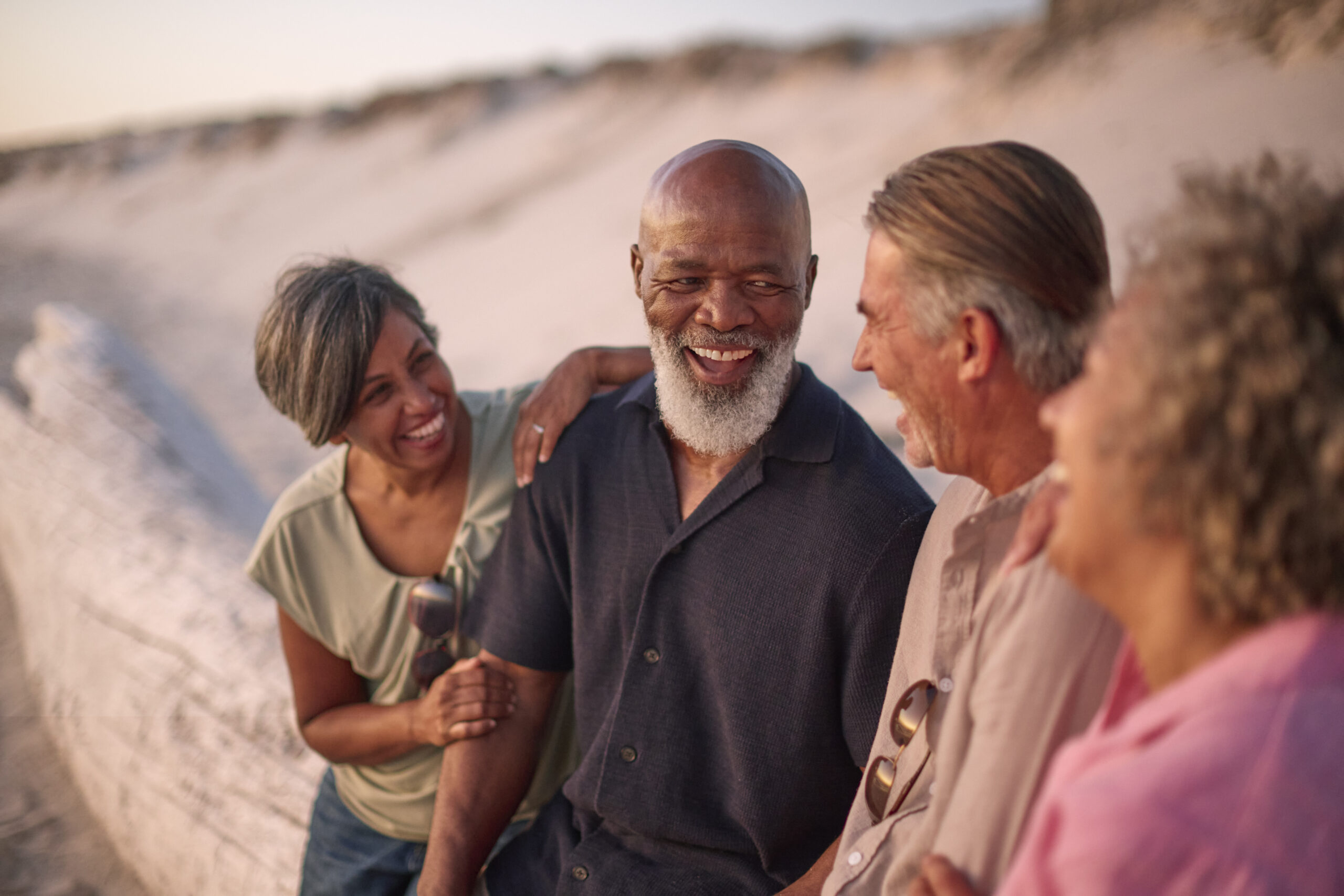 mature couple with friends sitting outdoors on beach watching sunset together